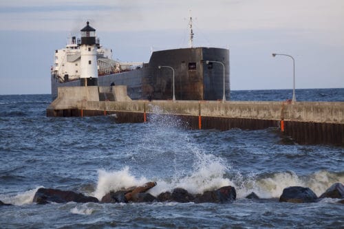 A freighter ship entering canal by lighthouse on Lake Superior.